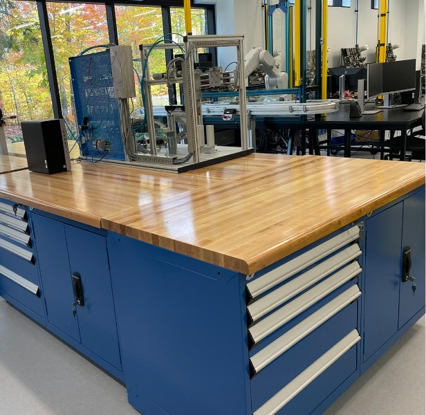 Industrial workstation with spacious wooden work surface and integrated blue tool cabinets with drawers for storage in a production environment.