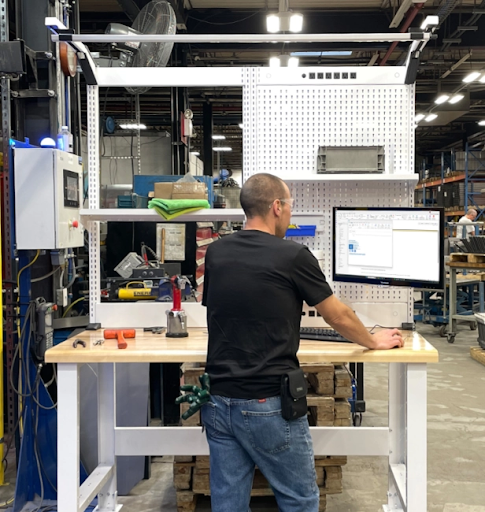 Établi industriel ajustable avec surface de travail en bois, utilisé par un opérateur dans un environnement de production.