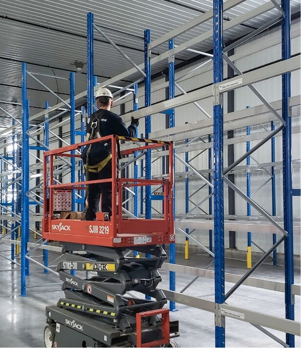Installation de racking industriel en acier avec technicien sur plateforme élévatrice dans un entrepôt
